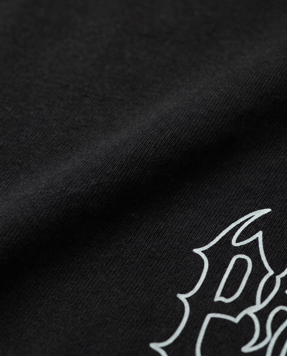 Macro da malha preta da camiseta Iron com parte do contorno claro da estampa PRISON®.