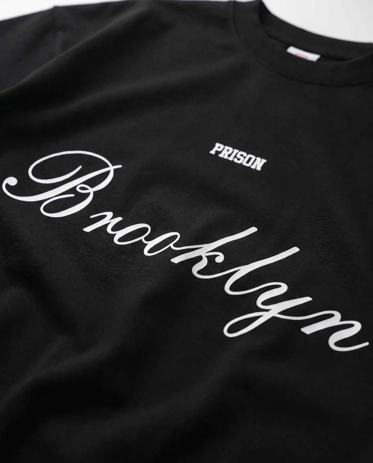 Detalhe do lettermark PRISON no peito da camiseta oversized preta