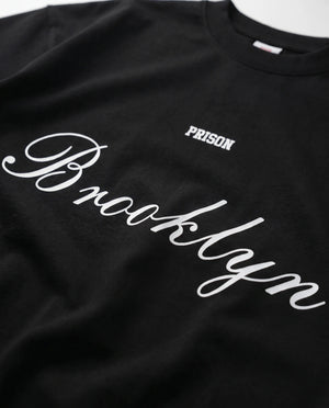 Detalhe do lettermark PRISON no peito da camiseta oversized preta