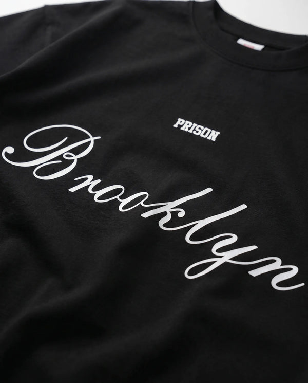Detalhe do lettermark PRISON no peito da camiseta oversized preta