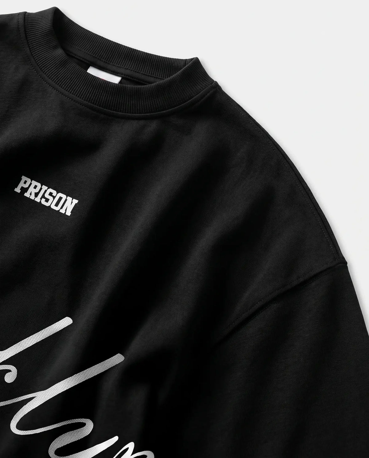Detalhe da gola canelada e do ombro caído da camiseta oversized preta Prison