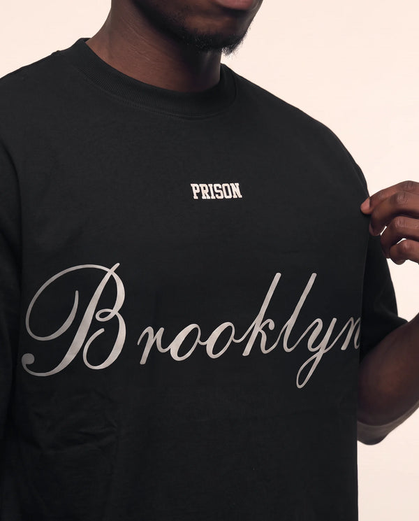 Detalhe do script Brooklyn na camiseta oversized preta masculina Prison