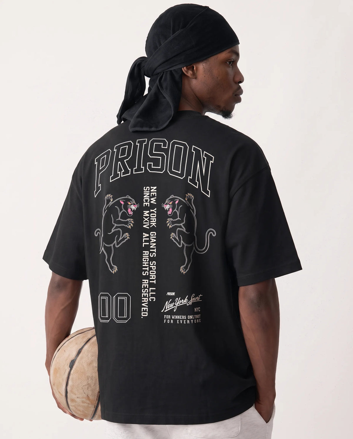 Modelo com bola de basquete vestindo a camiseta oversized NY Varsity Prison preta.