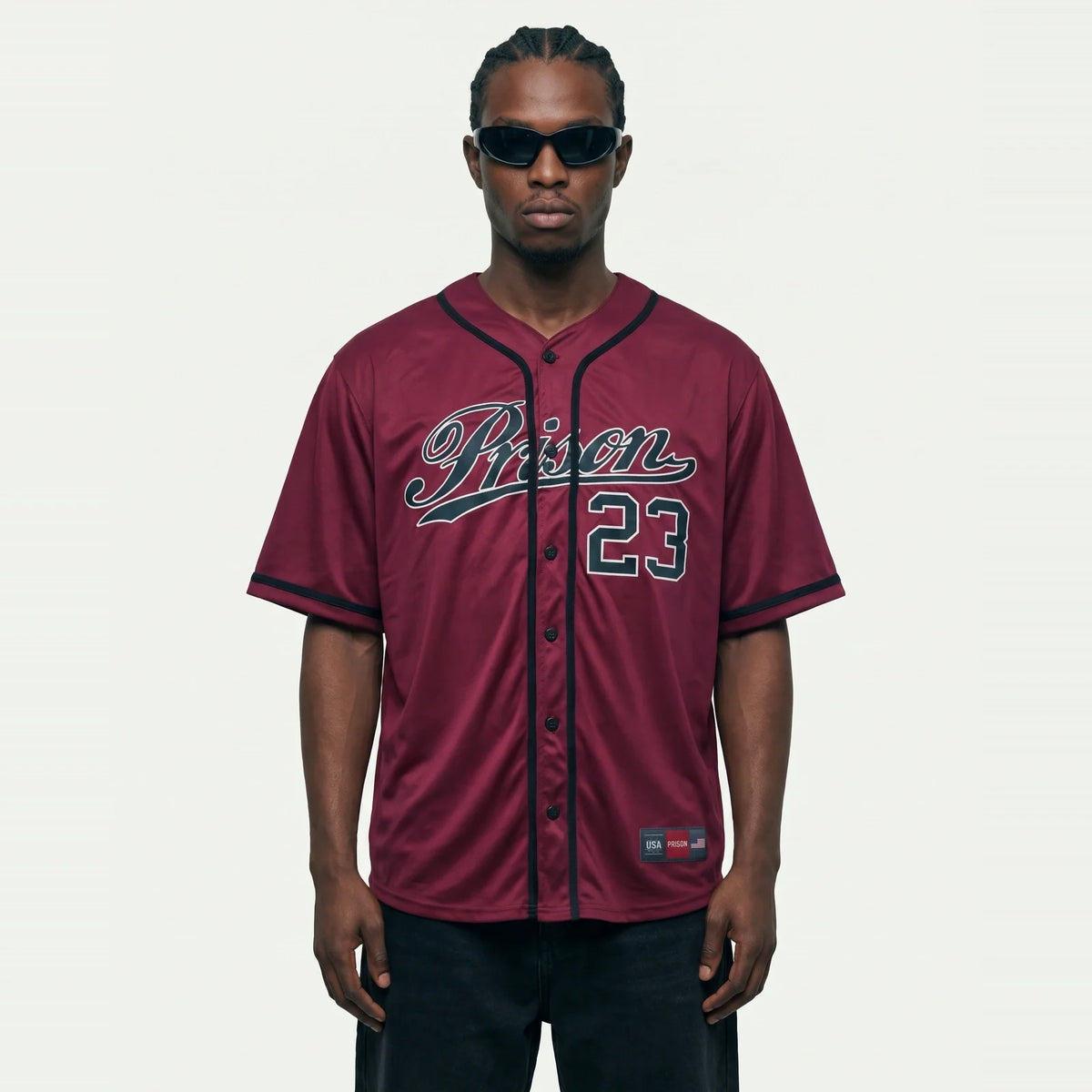 Jhon-1 veste a Camisa de Baseball Jersey 23 Vinho PRISON® de frente, com estampa Prison e 23 de contorno claro, calça preta e óculos escuros.