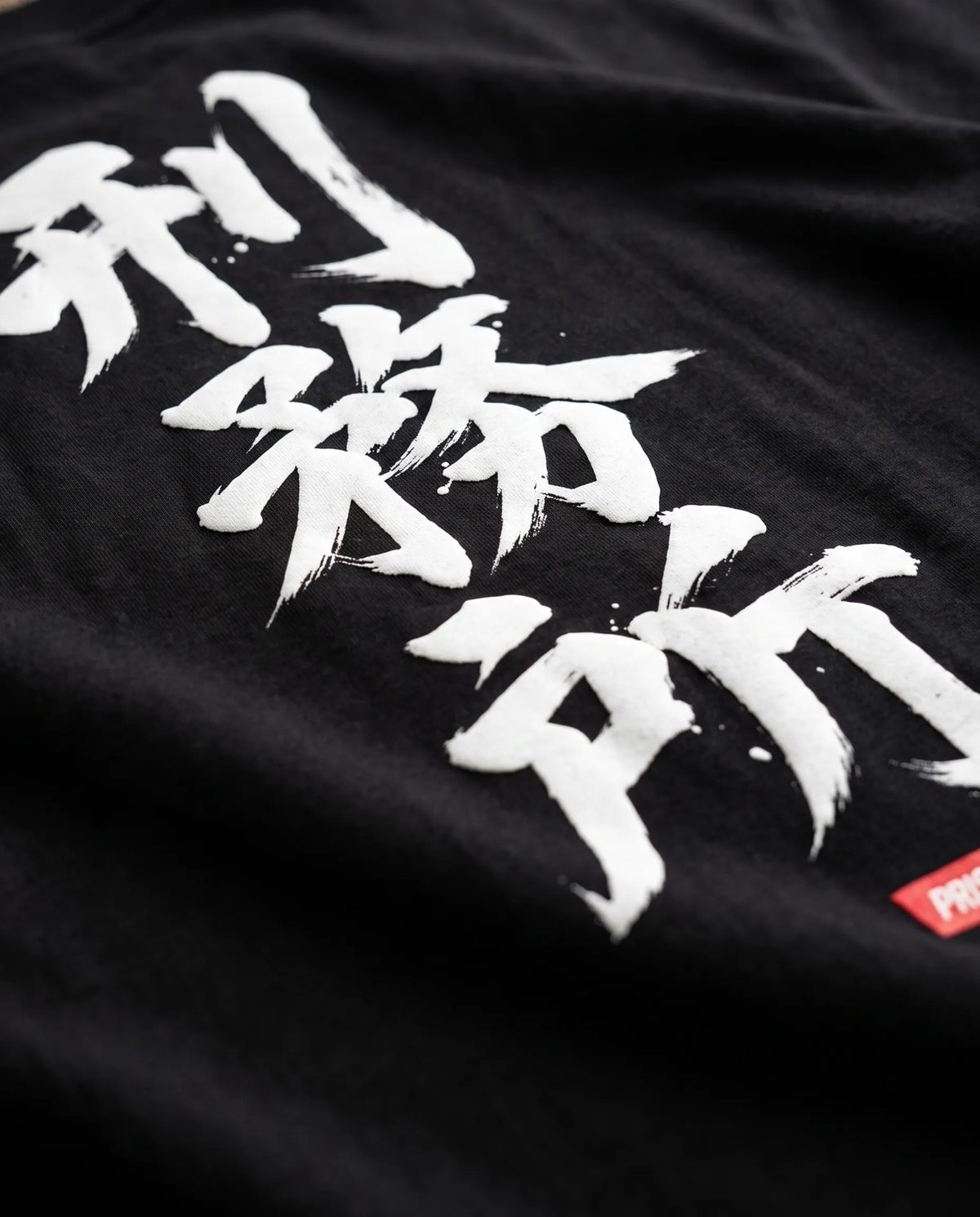 Detalhe da caligrafia em pincel branco com selo vermelho nas costas da camiseta oversized Prison.