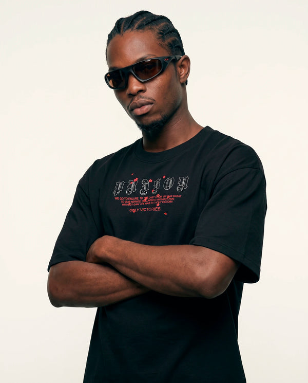 Modelo de braços cruzados vestindo a camiseta oversized Only Victories Prison preta.