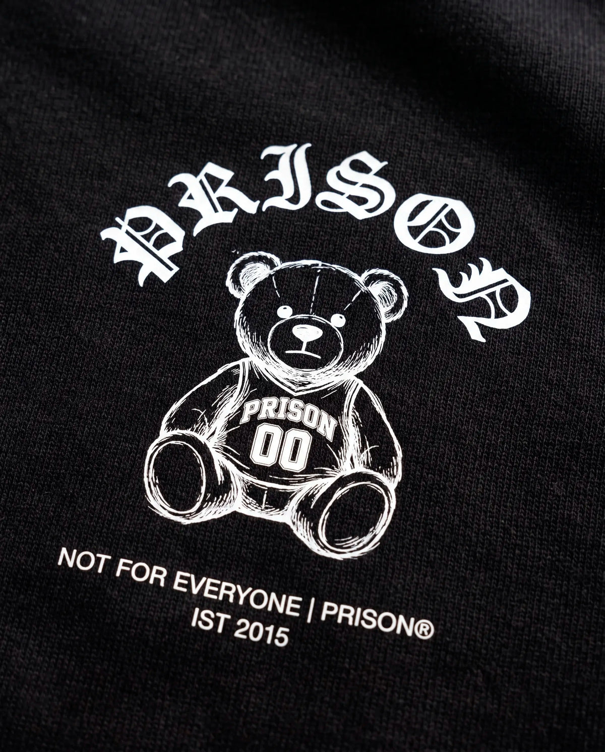 Detalhe da assinatura Not For Everyone e do urso no peito da camiseta oversized Prison preta.