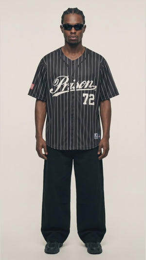 Vídeo de Jhon com a camisa de baseball Prison listrada preta em caimento oversized XXL, ombros levemente caídos e calça preta baggy, sem camiseta por baixo.