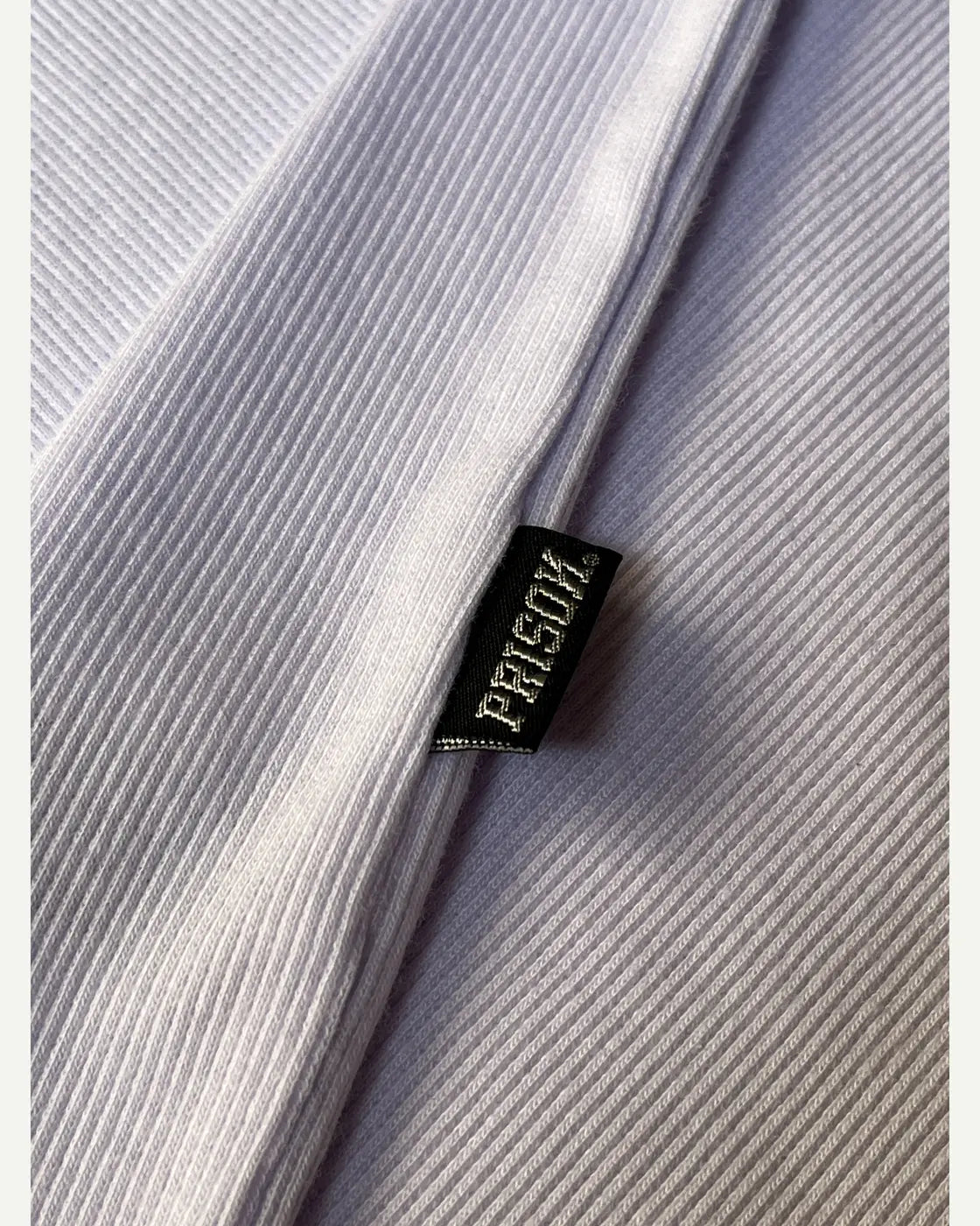 Detalhe real da etiqueta lateral PRISON® e da malha canelada branca.
