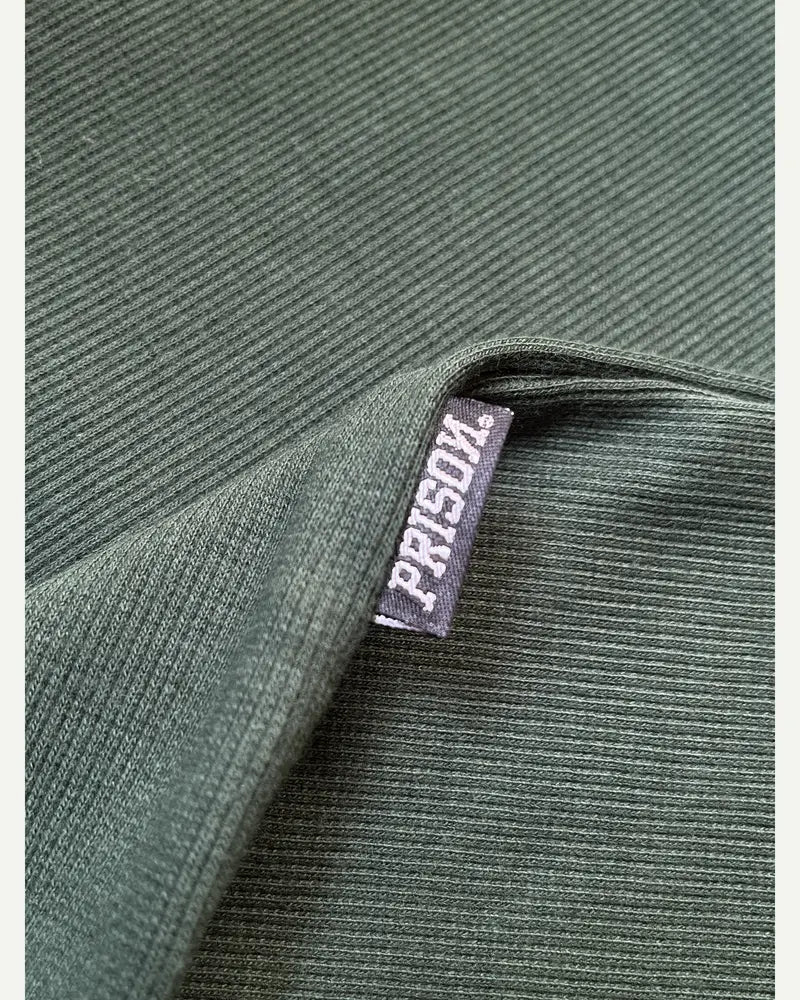 Detalhe real da etiqueta lateral PRISON® e do canelado verde militar.